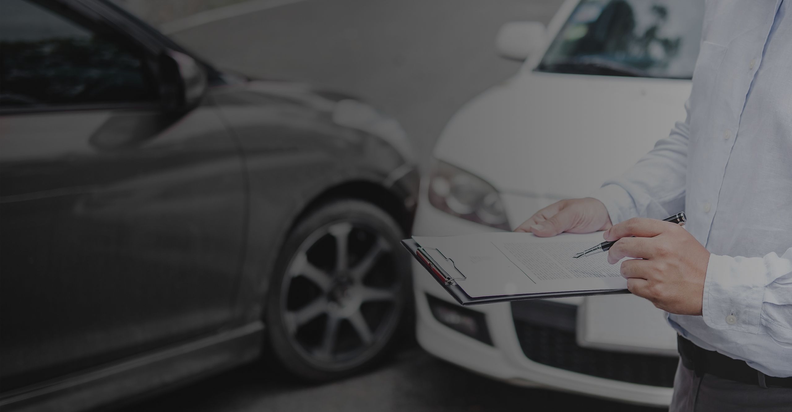 Ein Versicherungsvertreter dokumentiert den Schaden an einem verunfallten Auto mit einem Klemmbrett.